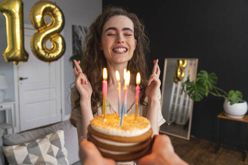 Young woman with fingers crossed in front of birthday cake at home - VPIF08026