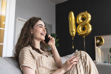 Cheerful young woman talking on phone celebrating birthday at home - VPIF08030