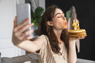 Eine junge Frau feiert ihren Geburtstag, indem sie die Kerzen auf ihrem Kuchen auspustet und den Moment mit einem Selfie festhält - VPIF08045