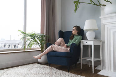 Nachdenkliche junge Frau entspannt sich auf einem Sessel zu Hause - VPIF08056