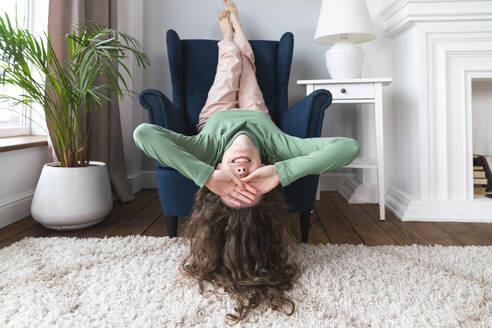 Woman covering eyes with feet up on armchair at home - VPIF08059