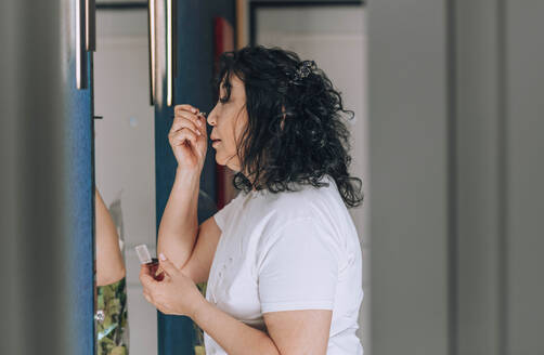 Frau trägt Wimperntusche auf und schaut in den Spiegel zu Hause - ADF00074