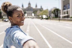 Eine glückliche Frau hält einen Moment der Freude an einem sonnigen Tag fest, indem sie ein Selfie auf der Straße macht - JCZF01244