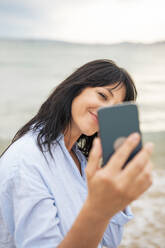 Eine Frau hält einen Moment am Strand mit einem Selfie fest, das sie mit ihrem Smartphone aufgenommen hat - JOSEF19153