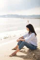 Smiling woman sitting on sand at beach - JOSEF19173