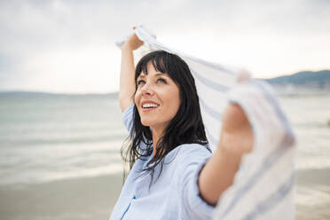 Mature woman day dreaming holding scarf at beach - JOSEF19198