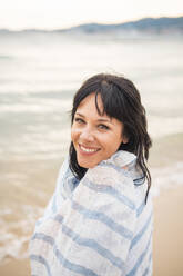 Smiling woman wrapped in scarf near sea at beach - JOSEF19208