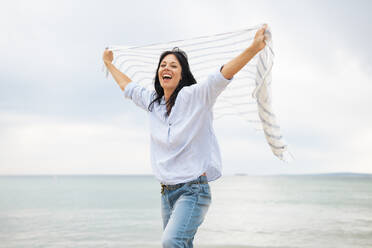 Glückliche Frau hält Schal und schreit am Strand - JOSEF19211