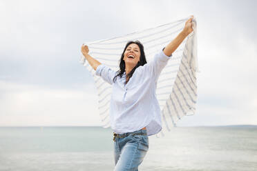 Carefree woman with scarf laughing at beach - JOSEF19212