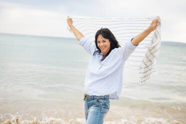 Lächelnde Frau mit erhobenen Armen und Schal am Strand - JOSEF19213