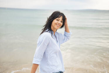 Smiling woman with hand in hair at beach - JOSEF19215