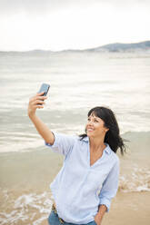 Eine glückliche Frau hält einen Moment am Strand mit einem Selfie mit ihrem Mobiltelefon fest - JOSEF19222