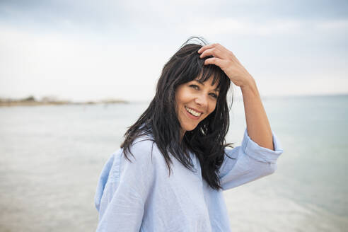 Smiling woman with hand in hair at beach - JOSEF19240