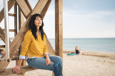 Mature woman sitting on lifeguard hut at beach - JOSEF19247