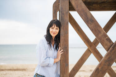 Smiling woman standing near lifeguard hut at beach - JOSEF19254