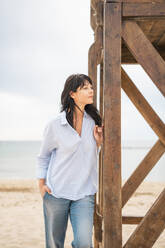 Thoughtful woman standing near lifeguard hut at beach - JOSEF19256