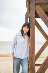 Smiling mature woman by lifeguard hut at beach - JOSEF19257