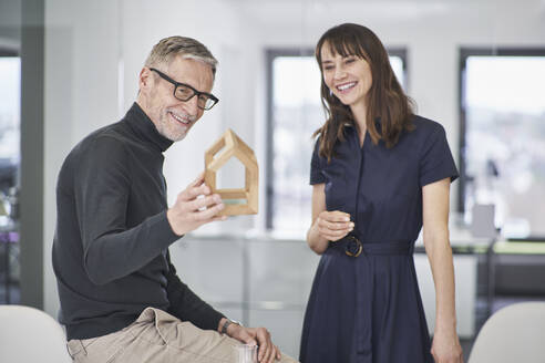 Zwei lächelnde Architekten betrachten ein Modellhaus im Büro - RORF03573