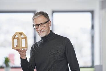 Portrait of senior architect holding model house in office - RORF03584