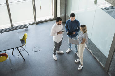 Businesswoman holding laptop discussing with colleagues in office - UUF28661