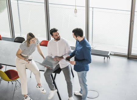 Businessman with laptop explaining to coworkers at workplace - UUF28668