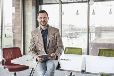 Selbstbewusster Geschäftsmann mit Tablet-PC auf dem Tisch im Büro - UUF28683