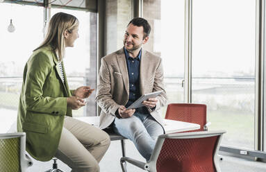 Businesswoman discussing with colleague holding tablet PC in office - UUF28686