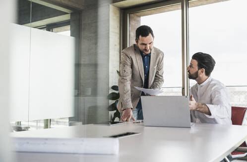 Businessman explaining to colleague over laptop at table - UUF28693