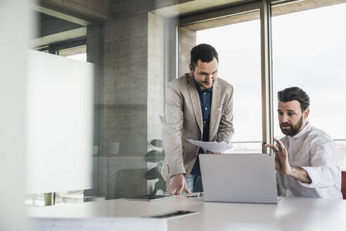 Businessman explaining to coworker over laptop at table - UUF28694