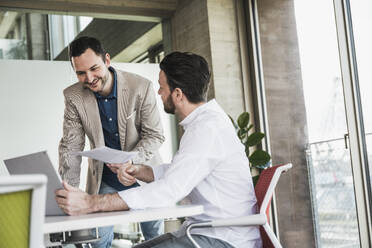 Colleague listening to businessman explaining over laptop at table - UUF28696