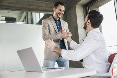 Business colleagues doing handshake with laptop at table - UUF28697