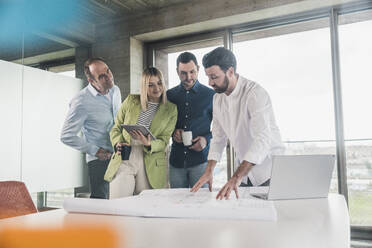 Businessman explaining blueprint to colleagues at table in office - UUF28705