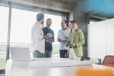 Businessman explaining to colleagues with laptop and blueprint on table - UUF28706