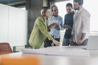 Businesswoman explaining blueprint to coworkers at table in office - UUF28708