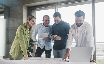 Smiling business colleagues examining blueprint at table in office - UUF28709