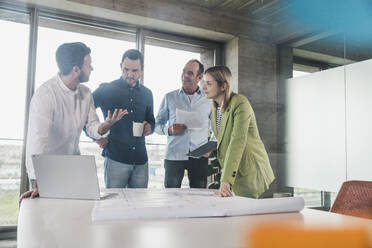 Businessman explaining to coworkers with laptop and blueprint at table - UUF28711