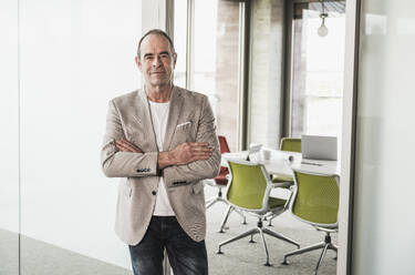 Confident businessman with arms crossed standing in office - UUF28737