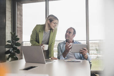 Businessman discussing with coworker over tablet PC at table in office - UUF28751