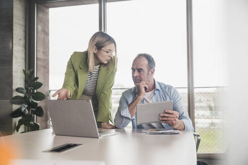 Businesswoman discussing with colleague over laptop at table in office - UUF28754
