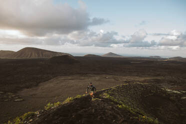 Distant tourist walking on grassy hill against picturesque scenery under cloudy sky in Lanzarote - ADSF44138