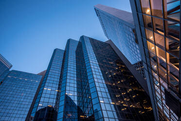 Von unten vom Eingang eines Bürogebäudes neben modernen Hochhäusern mit verspiegelten Glaswänden und beleuchteten Lichtern in Calgary gegen wolkenlosen blauen Himmel - ADSF44147
