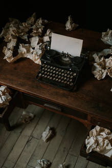 From above retro home office with wooden table and vintage typewriter near old lamp and many crumpled white papers - ADSF44159