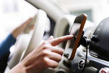 Crop anonymous female driver using navigator in smartphone while driving modern car with white steering wheel - ADSF44185