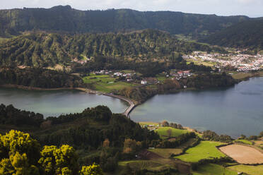 Drone Blick auf kleines Dorf auf grasbewachsenen Hügel in der Nähe von ruhigen See mit grünen Bäumen im Sommer Tag auf dem Land Azoren Portugal gelegen - ADSF44226