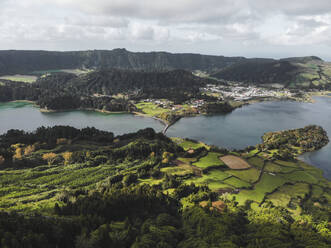 Landschaftliche Ansicht von Wohnsitzen und Siedlungen der Azoren-Region in der Nähe von grünen landwirtschaftlichen Feldern gegen ferne Berge und bewölkten Himmel in verschwommenem Tageslicht - ADSF44233