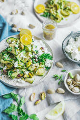 Top view of delicious healthy grilled courgette salad with feta cheese and pistachios served with slices on lemons and herbs on table - ADSF44237