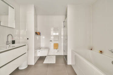 Interior design of clean contemporary restroom with white tiled walls and bathtub placed against sink and mirror - ADSF44258