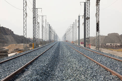Infrastrukturentwicklungsprojekt mit der Verlegung von Gleisen mit Oberleitungsmasten parallel zu Hochspannungsleitungen in trockenem Gelände während der Sommermonate - ADSF44326