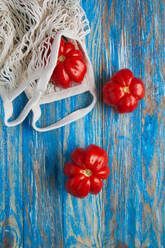 Draufsicht auf frische reife rote Tomaten mit umweltfreundlicher Baumwoll-Netztasche auf blau gestreiftem Holztisch - ADSF44333