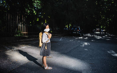 Portrait of small Japanese girl with backpack standing outdoors in town, coronavirus concept. Copy space. - HPIF15425